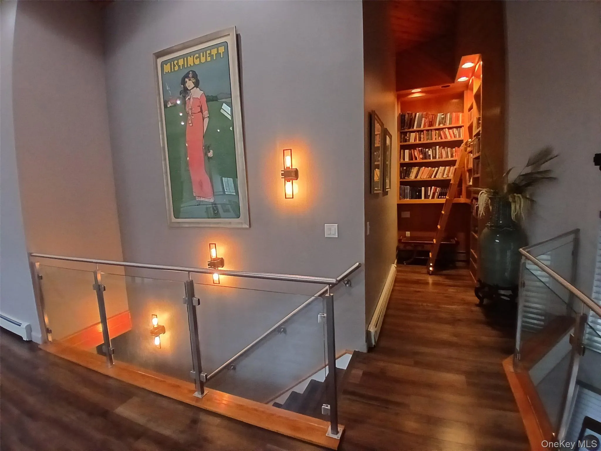 Wood-finish flooring, glass and metal railing, wall-mounted light fixtures, built-in library shelving, and a rolling library ladder Wood-finish flooring, glass and metal railing, wall-mounted light fixtures, built-in library shelving, and a rolling library ladder