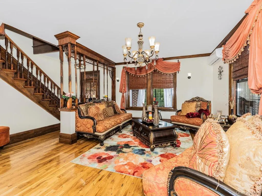 Living room with a wall mounted AC, ornamental molding, a notable chandelier, and hardwood / wood-style floors Living room with a wall mounted AC, ornamental molding, a notable chandelier, and hardwood / wood-style floors