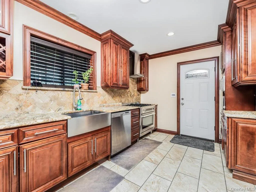 Kitchen with range, light tile patterned floors, wall chimney range hood, dishwasher, and light stone countertops Kitchen with range, light tile patterned floors, wall chimney range hood, dishwasher, and light stone countertops