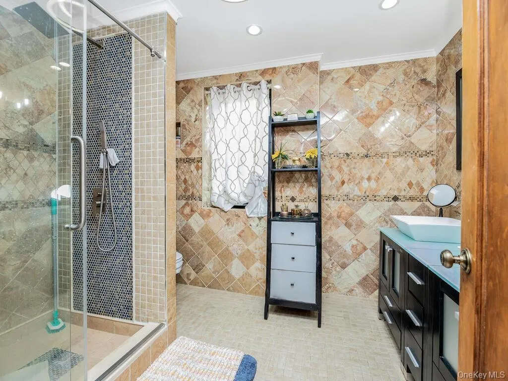 Bathroom featuring tile patterned flooring, an enclosed shower, toilet, vanity, and tile walls Bathroom featuring tile patterned flooring, an enclosed shower, toilet, vanity, and tile walls