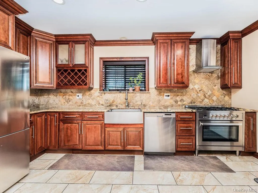 Kitchen with appliances with stainless steel finishes, light tile patterned flooring, sink, and wall chimney exhaust hood Kitchen with appliances with stainless steel finishes, light tile patterned flooring, sink, and wall chimney exhaust hood