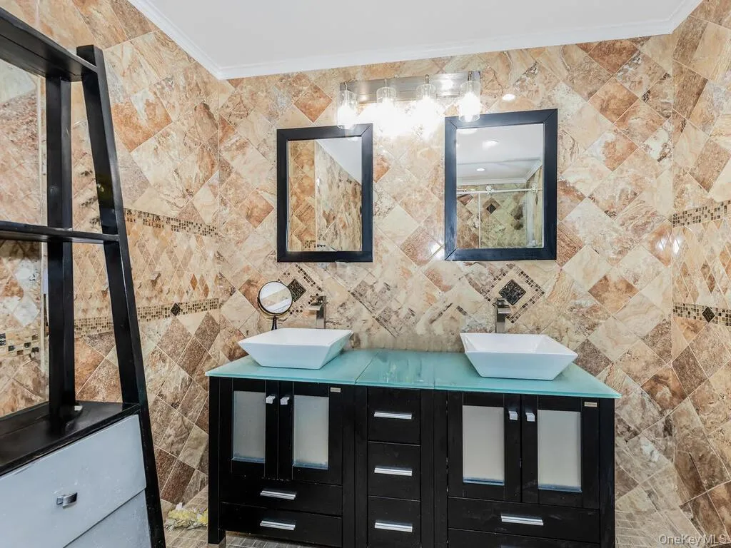 Bathroom featuring tile walls, dual vanity, and crown molding Bathroom featuring tile walls, dual vanity, and crown molding