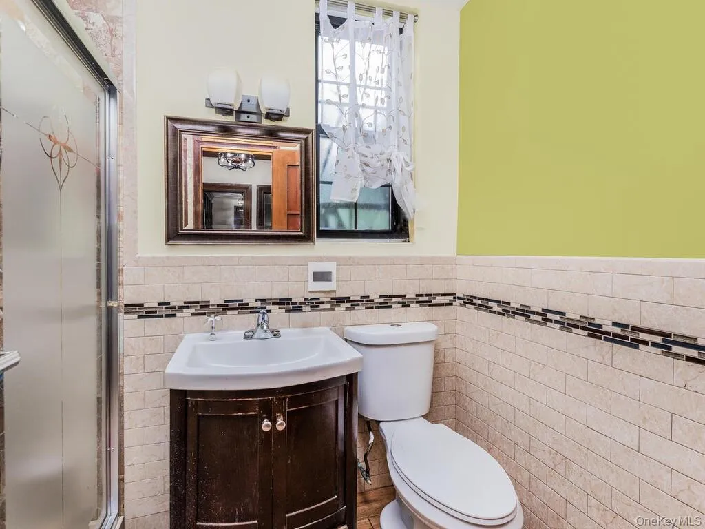 Bathroom featuring tile walls, a shower with door, toilet, and vanity Bathroom featuring tile walls, a shower with door, toilet, and vanity