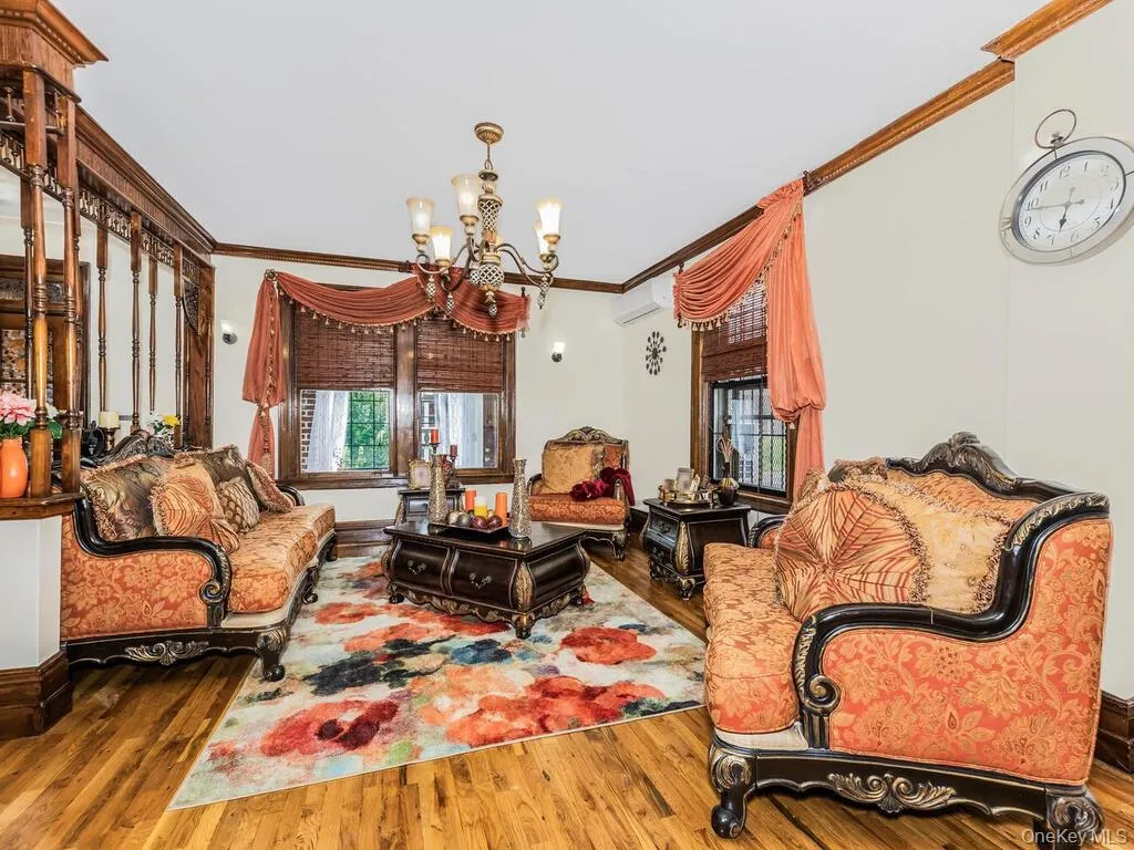 Living room featuring a wall unit AC, a notable chandelier, ornamental molding, and wood-type flooring Living room featuring a wall unit AC, a notable chandelier, ornamental molding, and wood-type flooring
