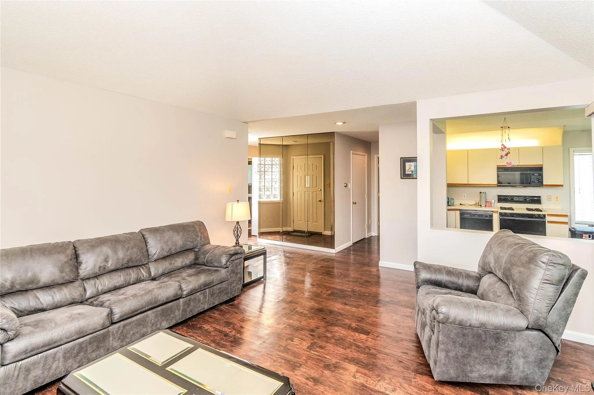 Wood-finish flooring throughout, with a framed opening to the kitchen featuring light-toned cabinetry and built-in appliances Wood-finish flooring throughout, with a framed opening to the kitchen featuring light-toned cabinetry and built-in appliances