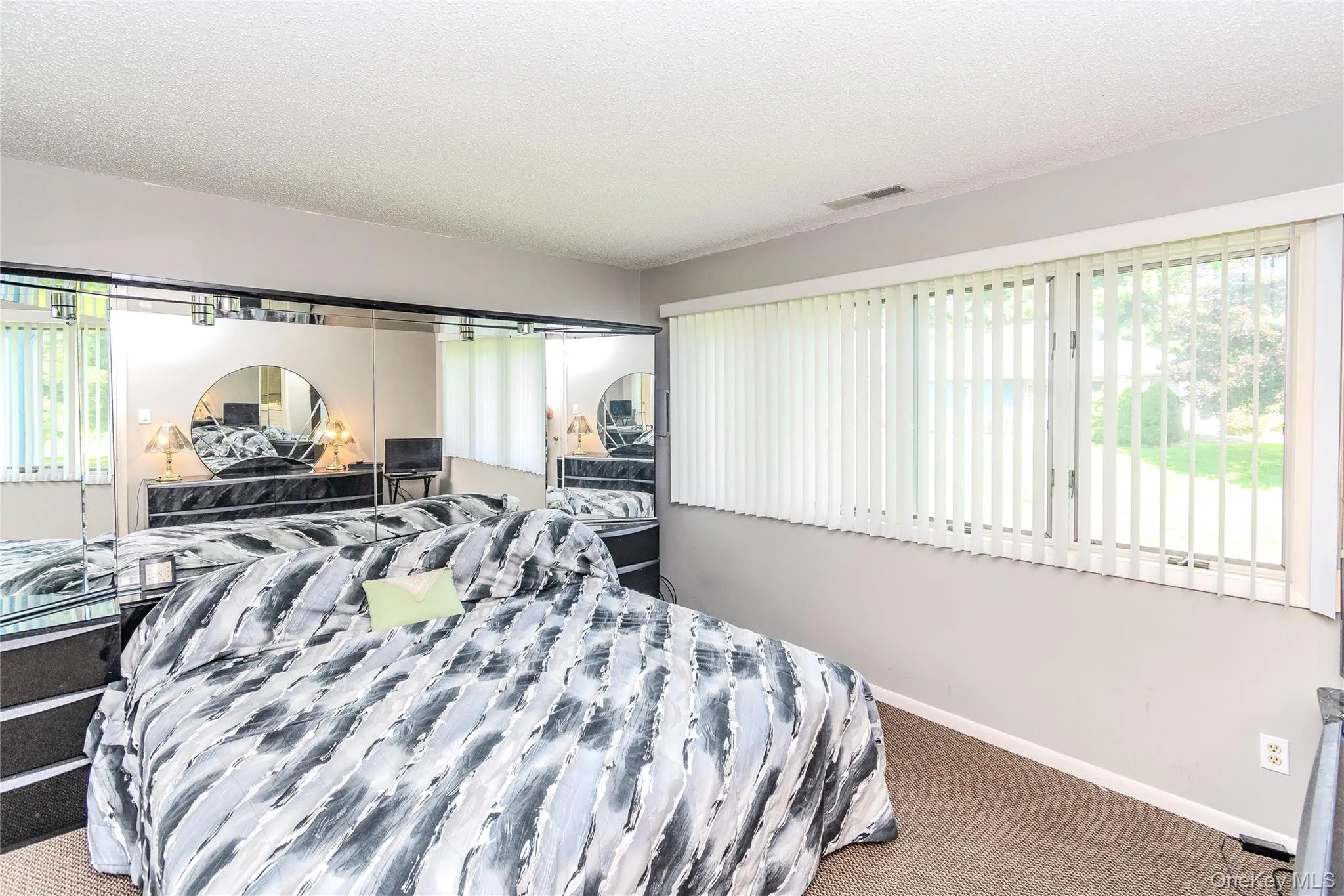 Mirrored closet doors, carpeted flooring, and a large window with vertical blinds Mirrored closet doors, carpeted flooring, and a large window with vertical blinds