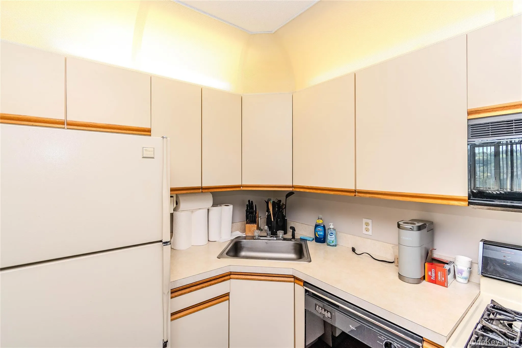 Kitchen featuring light-toned cabinetry with wood trim, a stainless steel sink, and light-toned countertops Kitchen featuring light-toned cabinetry with wood trim, a stainless steel sink, and light-toned countertops