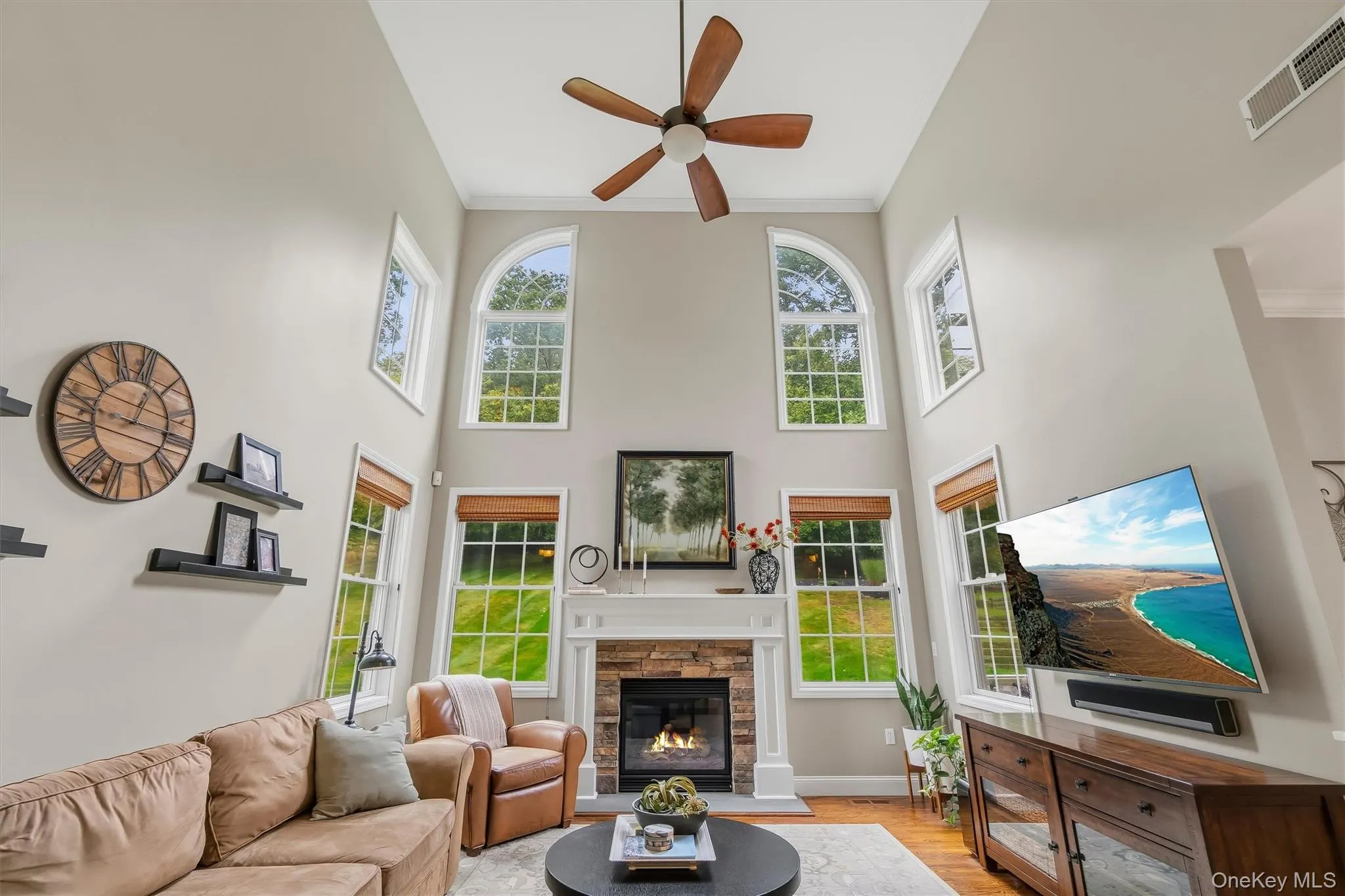 Bathed in natural light from a dramatic wall of windows, this impressive family room offers an open, airy atmosphere beneath a soaring two-story ceiling. The striking 36-inch gas fireplace is surrounded by stacked stone and crowned with an oversized wood mantel, creating a warm and memorable centerpiece. Gleaming hardwood floors, custom blinds, and a ceiling fan add comfort and character to this beautifully designed gathering space. Bathed in natural light from a dramatic wall of windows, this impressive family room offers an open, airy atmosphere beneath a soaring two-story ceiling. The striking 36-inch gas fireplace is surrounded by stacked stone and crowned with an oversized wood mantel, creating a warm and memorable centerpiece. Gleaming hardwood floors, custom blinds, and a ceiling fan add comfort and character to this beautifully designed gathering space.
