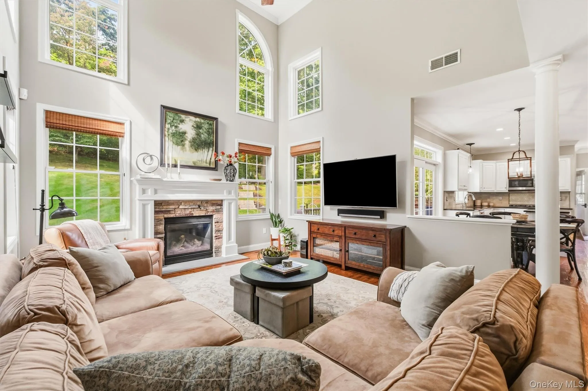 This expansive family room makes a striking impression with its soaring two-story ceiling and dramatic wall of windows. A 36-inch gas fireplace, framed by stacked stone and topped with an oversized wood mantel, creates a stunning focal point, while gleaming hardwood floors, custom blinds, and a ceiling fan complete the warm and inviting space. This expansive family room makes a striking impression with its soaring two-story ceiling and dramatic wall of windows. A 36-inch gas fireplace, framed by stacked stone and topped with an oversized wood mantel, creates a stunning focal point, while gleaming hardwood floors, custom blinds, and a ceiling fan complete the warm and inviting space.