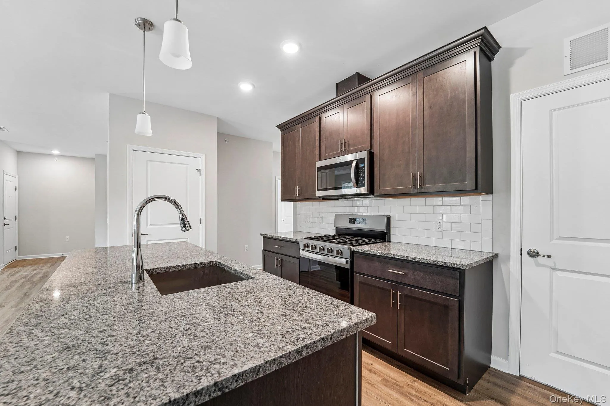 Kitchen featuring a stainless steel gas range, microwave, wood-finish cabinetry, and light-toned tile backsplash Kitchen featuring a stainless steel gas range, microwave, wood-finish cabinetry, and light-toned tile backsplash