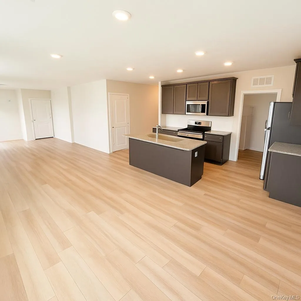 Open-concept living space featuring wood-finish flooring, recessed lighting, and a kitchen with dark cabinetry, stainless steel appliances, and a central island with a sink Open-concept living space featuring wood-finish flooring, recessed lighting, and a kitchen with dark cabinetry, stainless steel appliances, and a central island with a sink