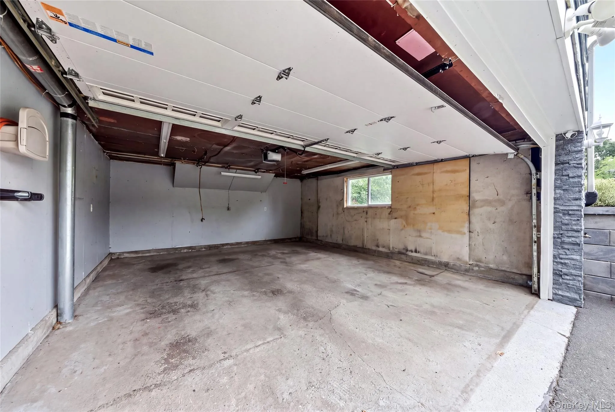 Spacious garage with concrete flooring, overhead lighting, and a single window Spacious garage with concrete flooring, overhead lighting, and a single window