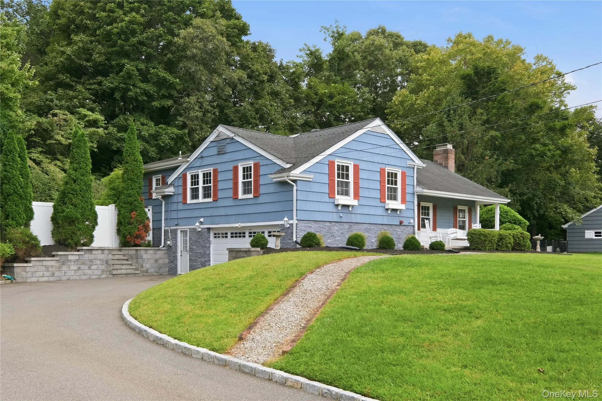 Blue siding exterior with contrasting red shutters, attached 1 1/2 car garage with white door, paved driveway, stone retaining walls, and established landscaping Blue siding exterior with contrasting red shutters, attached 1 1/2 car garage with white door, paved driveway, stone retaining walls, and established landscaping