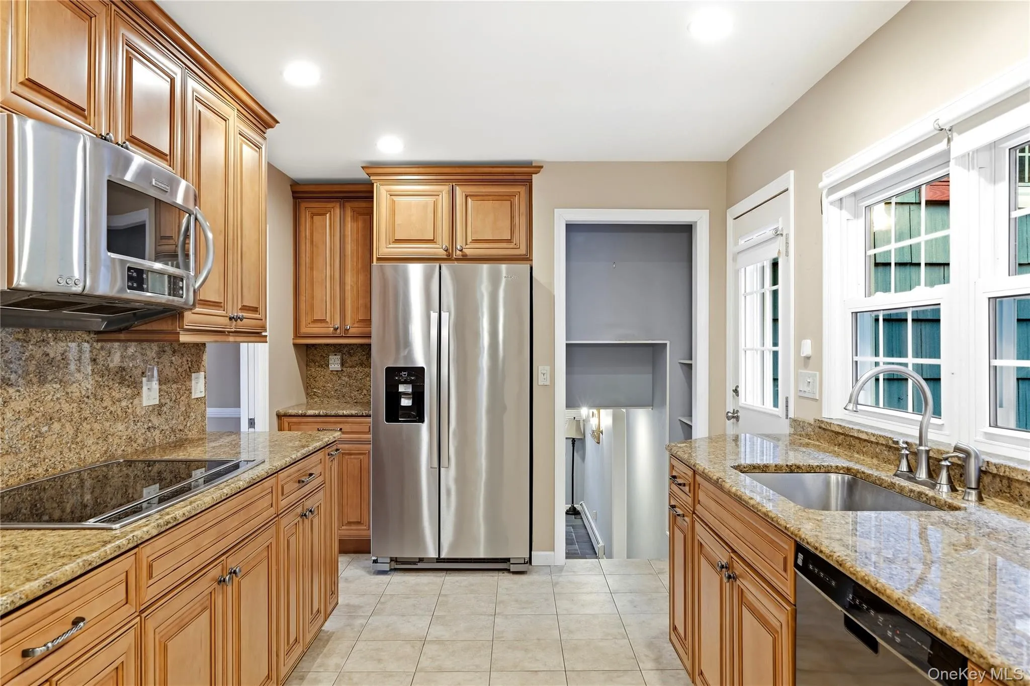 Kitchen featuring wood cabinetry, stainless steel appliances, granite countertops, and tiled flooring Kitchen featuring wood cabinetry, stainless steel appliances, granite countertops, and tiled flooring
