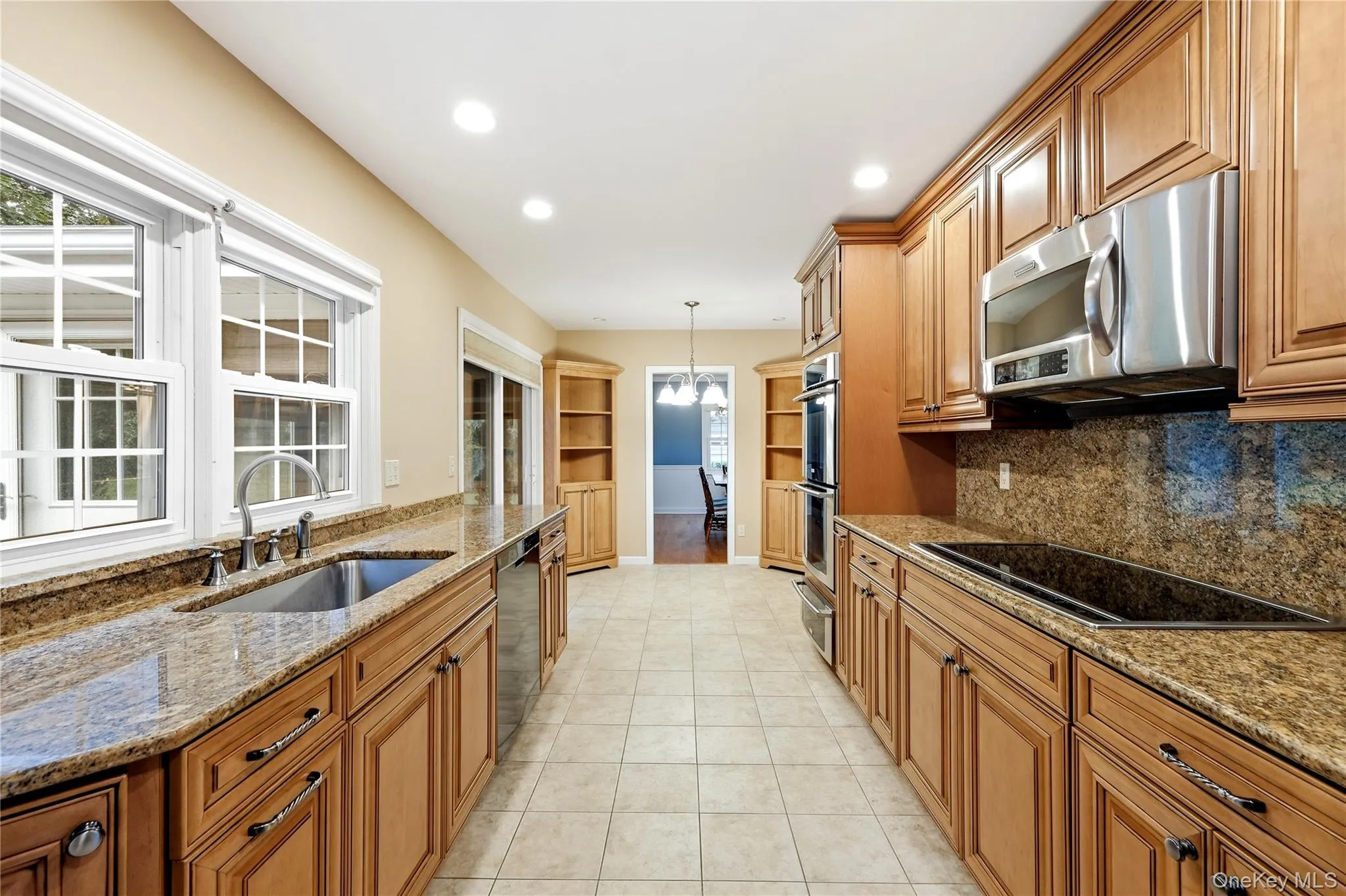 Kitchen featuring wood cabinetry, stainless steel appliances, a built-in cooktop, and light-toned tile flooring Kitchen featuring wood cabinetry, stainless steel appliances, a built-in cooktop, and light-toned tile flooring