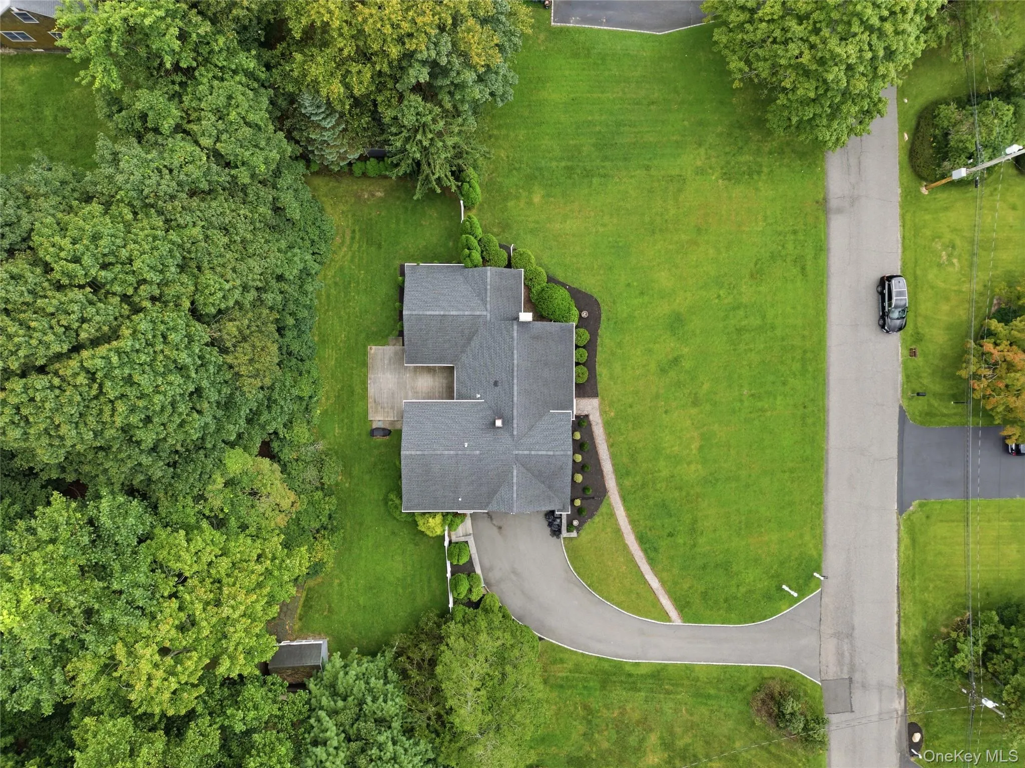 Expansive lawn surrounding the property, mature trees providing natural privacy, asphalt shingle roofing, paved driveway, and a wood-finish deck Expansive lawn surrounding the property, mature trees providing natural privacy, asphalt shingle roofing, paved driveway, and a wood-finish deck