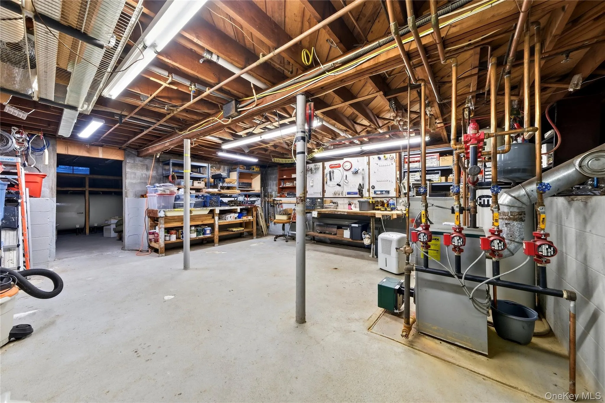 Unfinished basement featuring exposed wood ceiling joists, concrete flooring, and multiple utility systems Unfinished basement featuring exposed wood ceiling joists, concrete flooring, and multiple utility systems