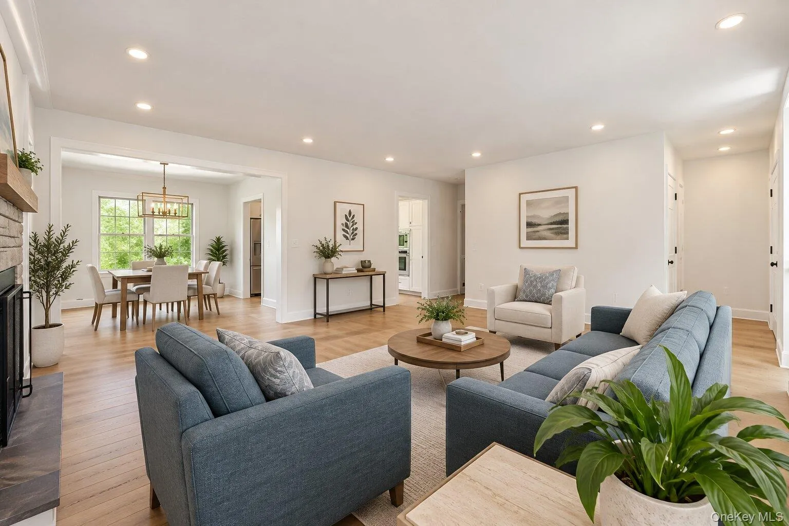 Expansive living area featuring light wood-finish flooring, recessed lighting, and a stone-clad fireplace with a wood mantel Expansive living area featuring light wood-finish flooring, recessed lighting, and a stone-clad fireplace with a wood mantel