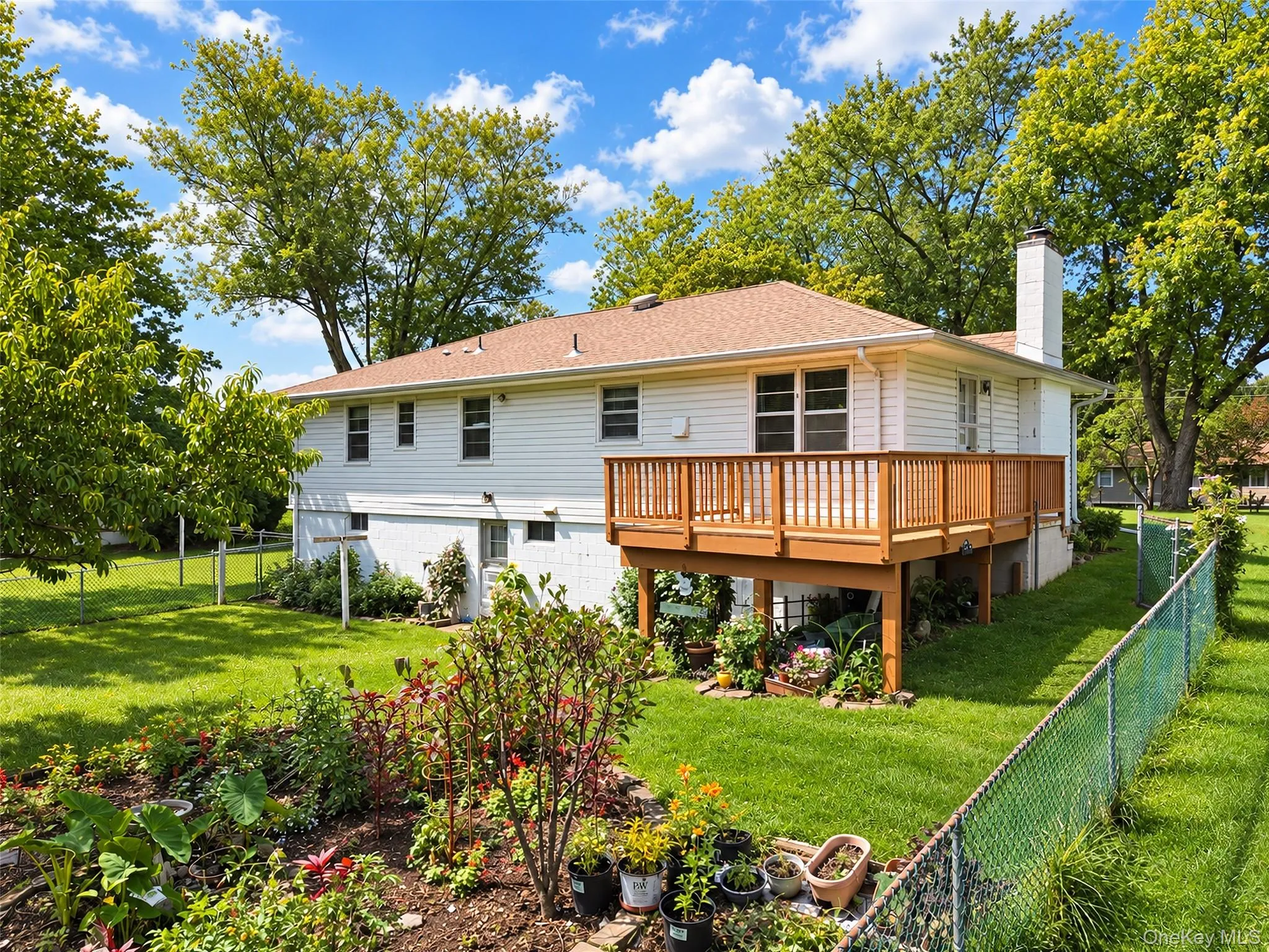 Expansive green lawn, elevated wood deck with railing, white siding exterior, brown shingle roof, and mature perimeter trees Expansive green lawn, elevated wood deck with railing, white siding exterior, brown shingle roof, and mature perimeter trees