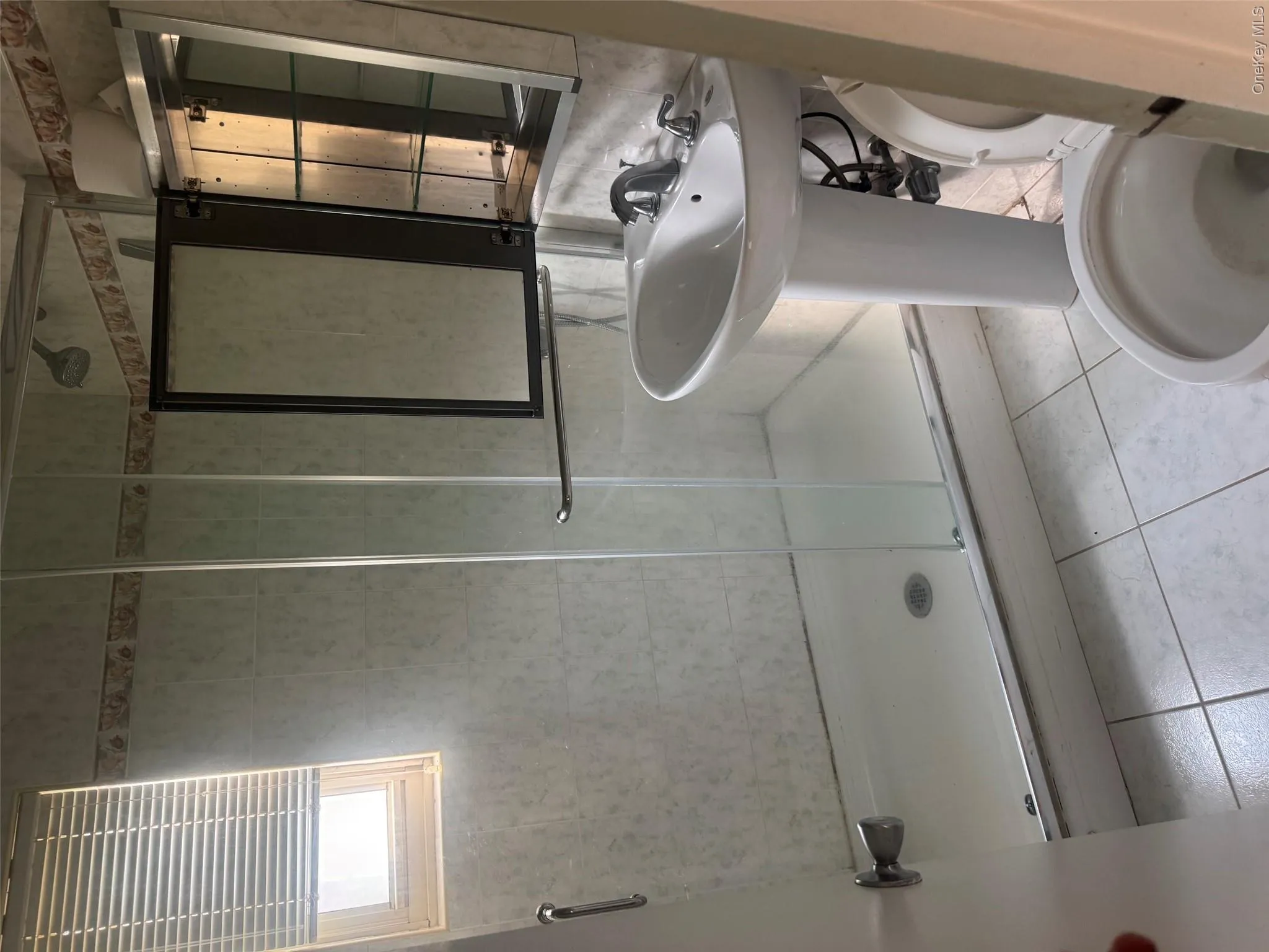 Pedestal sink with chrome faucet, tiled shower with glass enclosure, wall-mounted medicine cabinet, and tiled flooring Pedestal sink with chrome faucet, tiled shower with glass enclosure, wall-mounted medicine cabinet, and tiled flooring