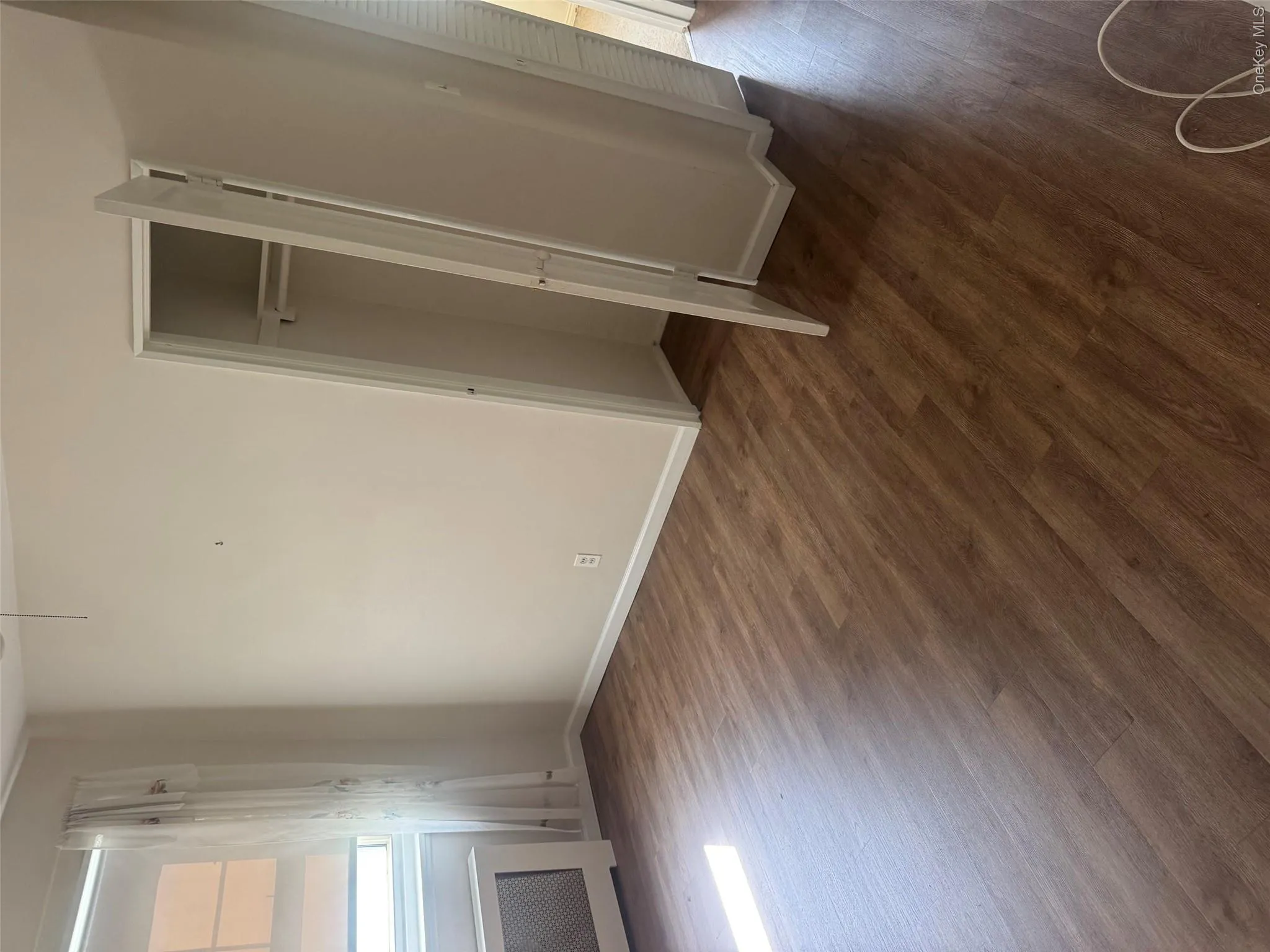 Wood-finish flooring, built-in closet with bi-fold doors, white trim, and a window with a radiator cover Wood-finish flooring, built-in closet with bi-fold doors, white trim, and a window with a radiator cover