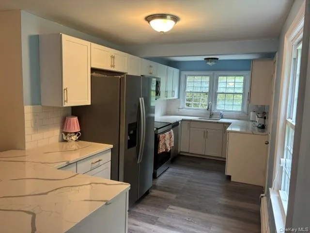 White cabinetry with gold-tone hardware, stainless steel appliances, white subway tile backsplash, quartz countertops, and laminate flooring White cabinetry with gold-tone hardware, stainless steel appliances, white subway tile backsplash, quartz countertops, and laminate flooring