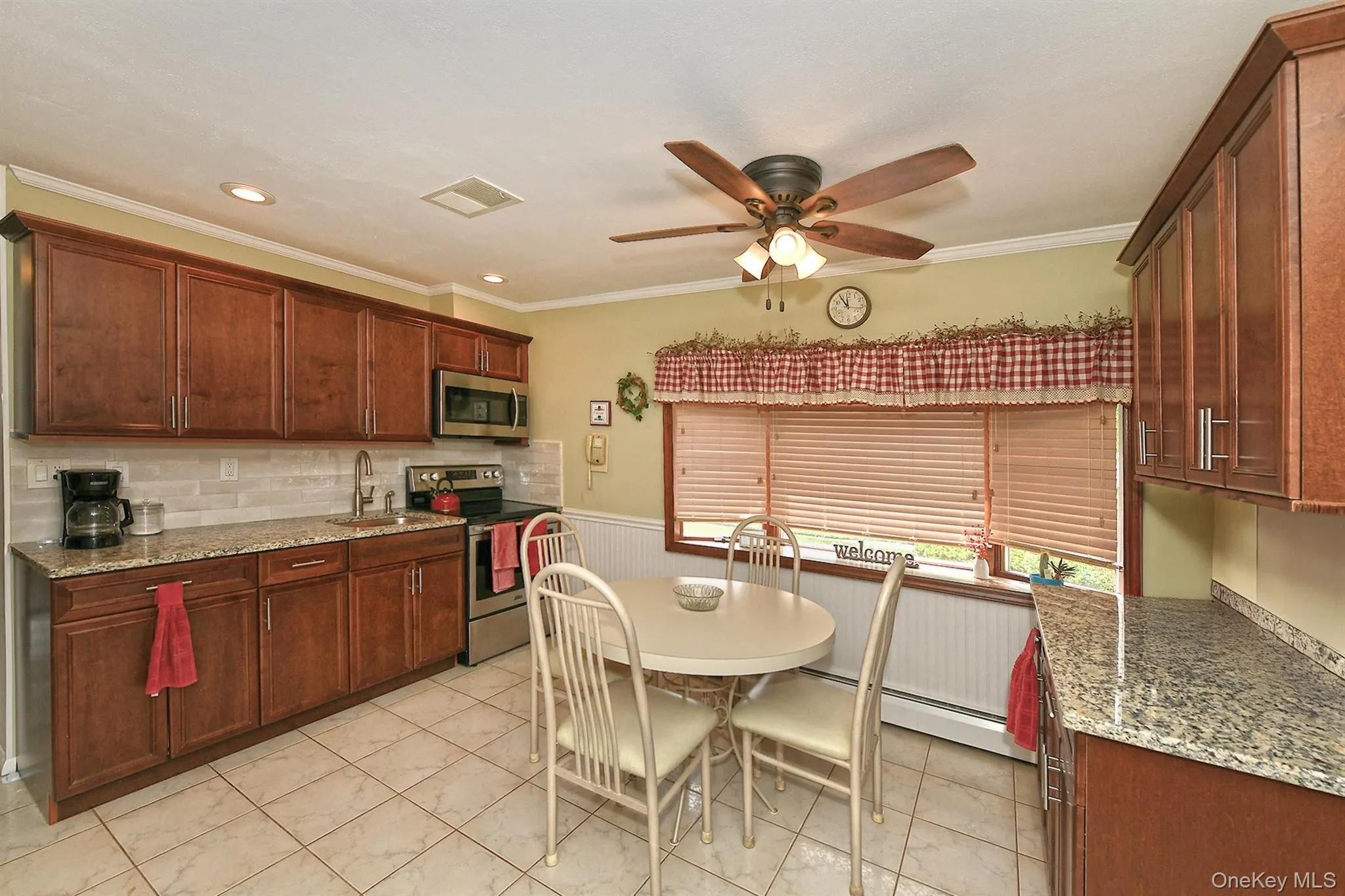 Kitchen featuring ceramic tile flooring, wood-finish cabinetry, light-toned countertops, tile backsplash, and a ceiling fan with integrated lighting Kitchen featuring ceramic tile flooring, wood-finish cabinetry, light-toned countertops, tile backsplash, and a ceiling fan with integrated lighting