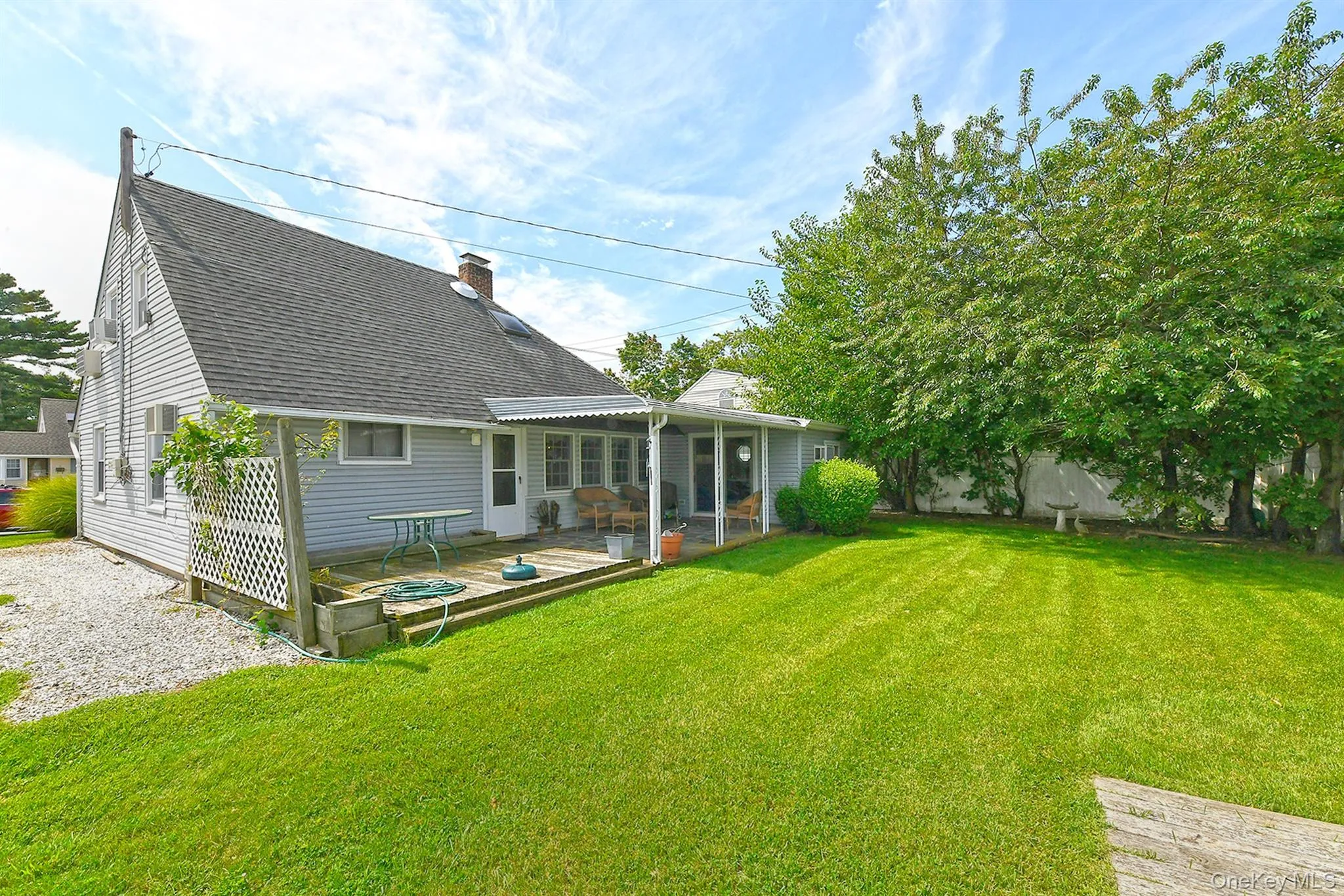 Expansive green lawn, wood deck, covered patio, white siding, and a gabled roof Expansive green lawn, wood deck, covered patio, white siding, and a gabled roof