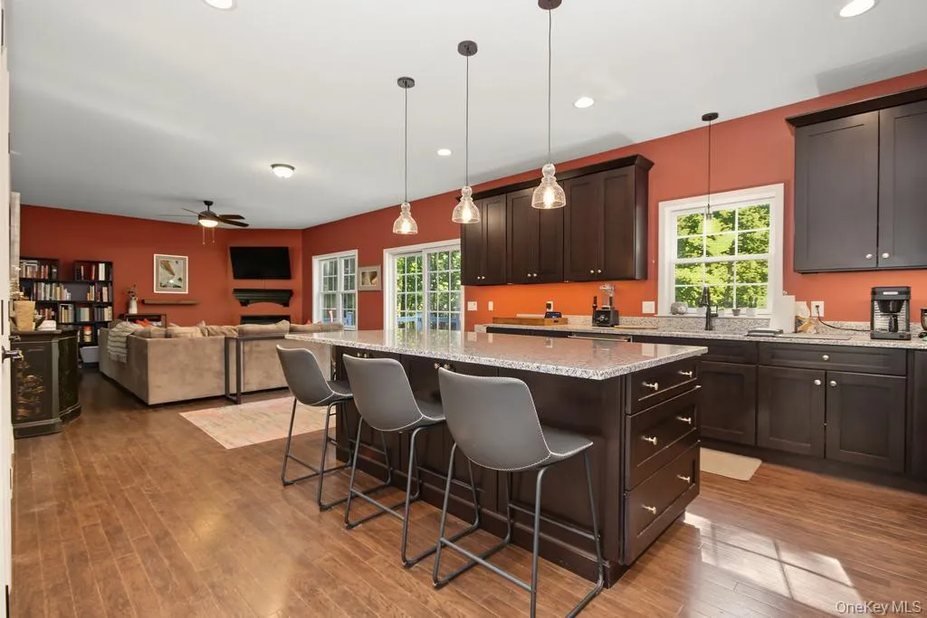 Open-concept kitchen and living area featuring wood-finish flooring, dark wood cabinetry, a center island with a light-toned countertop, and recessed lighting Open-concept kitchen and living area featuring wood-finish flooring, dark wood cabinetry, a center island with a light-toned countertop, and recessed lighting