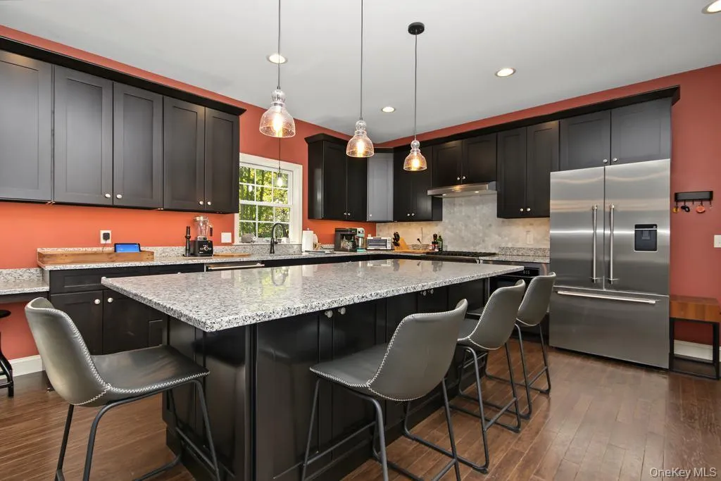 Spacious kitchen featuring dark cabinetry, stainless steel appliances, a large center island with a stone countertop, and wood-finish flooring Spacious kitchen featuring dark cabinetry, stainless steel appliances, a large center island with a stone countertop, and wood-finish flooring