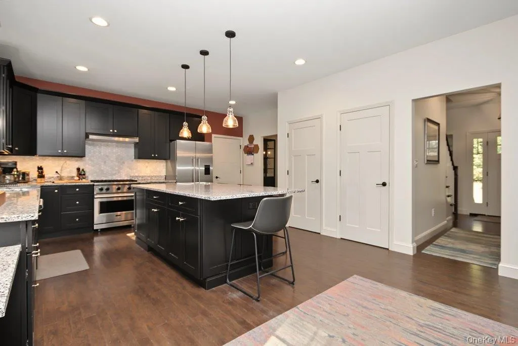Kitchen featuring dark wood-finish flooring, black cabinetry, stone countertops, stainless steel appliances, and pendant lighting Kitchen featuring dark wood-finish flooring, black cabinetry, stone countertops, stainless steel appliances, and pendant lighting