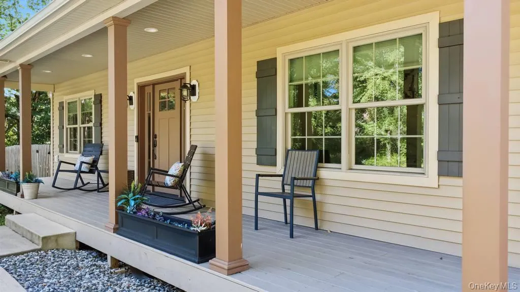 Expansive covered front porch with multiple support columns, light-toned siding, and dark shutters Expansive covered front porch with multiple support columns, light-toned siding, and dark shutters