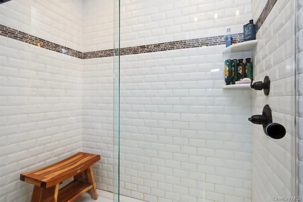 White subway tile shower with a mosaic tile accent band, integrated corner shelving, and oil-rubbed bronze fixtures White subway tile shower with a mosaic tile accent band, integrated corner shelving, and oil-rubbed bronze fixtures