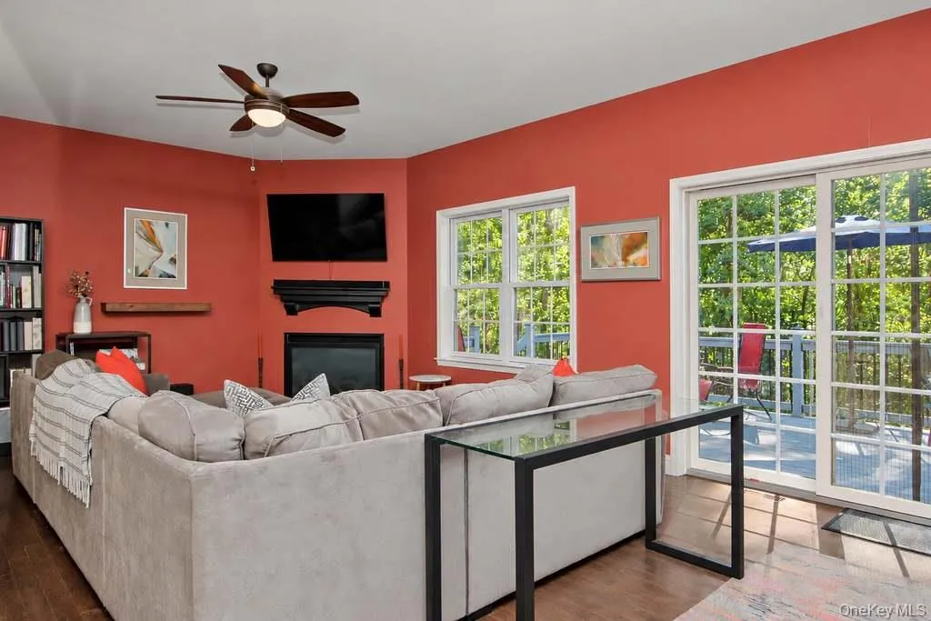 Corner fireplace with a mantel, wood-finish flooring, white-framed windows, and sliding glass doors to the exterior Corner fireplace with a mantel, wood-finish flooring, white-framed windows, and sliding glass doors to the exterior