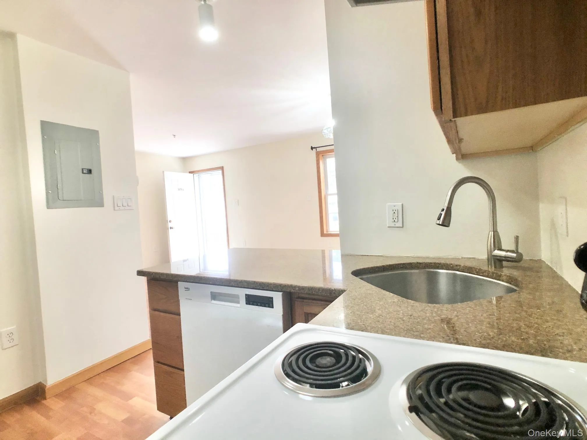 Kitchen with a peninsula, dark stone counters, electric panel, white appliances, and light wood-style floors Kitchen with a peninsula, dark stone counters, electric panel, white appliances, and light wood-style floors