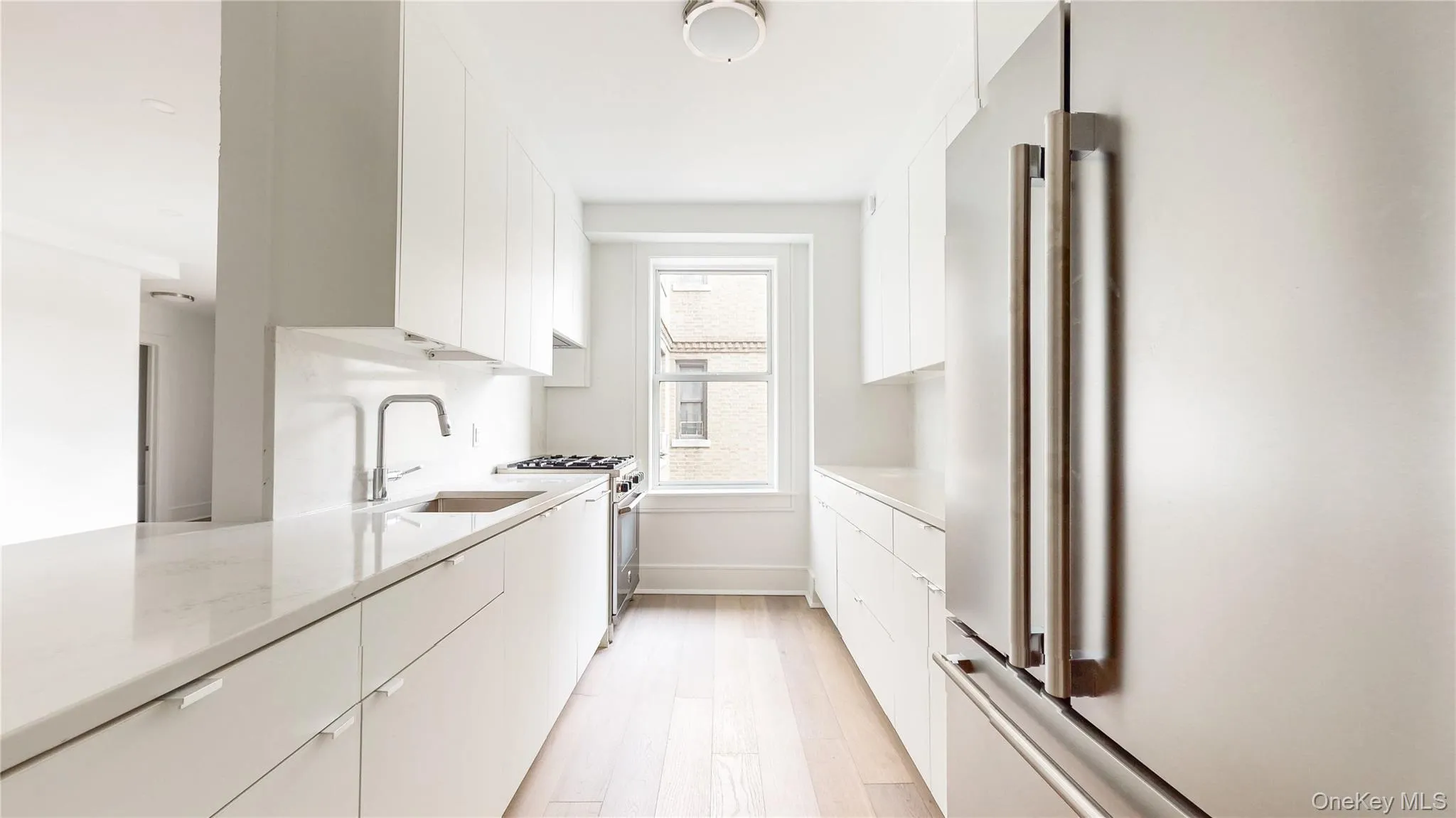 Galley kitchen featuring white cabinetry, light-toned wood-finish flooring, stainless steel appliances, and a window Galley kitchen featuring white cabinetry, light-toned wood-finish flooring, stainless steel appliances, and a window