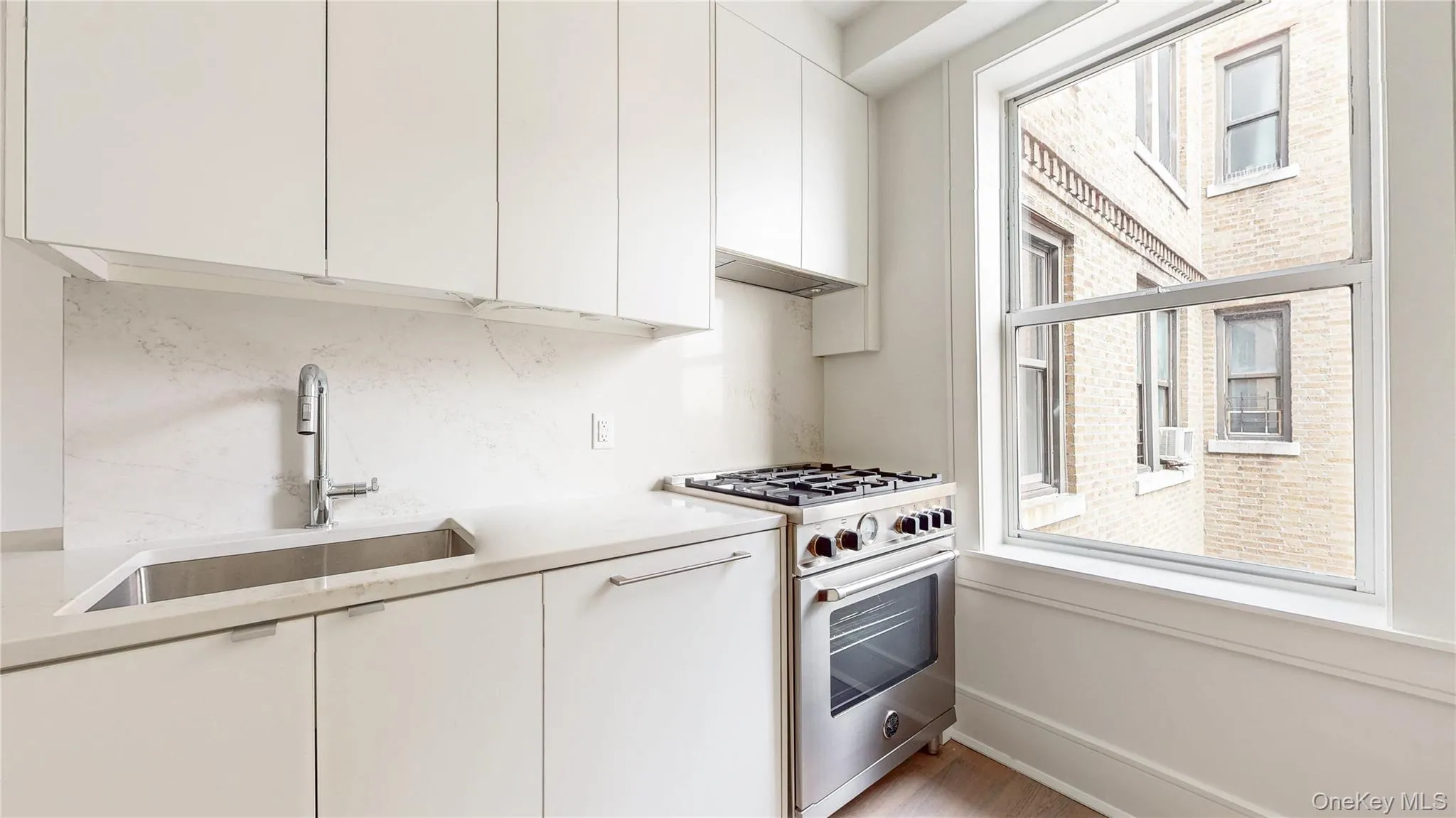 Modern kitchen featuring white cabinetry, integrated stainless steel sink, stainless steel range, light-toned countertops, and a large window Modern kitchen featuring white cabinetry, integrated stainless steel sink, stainless steel range, light-toned countertops, and a large window