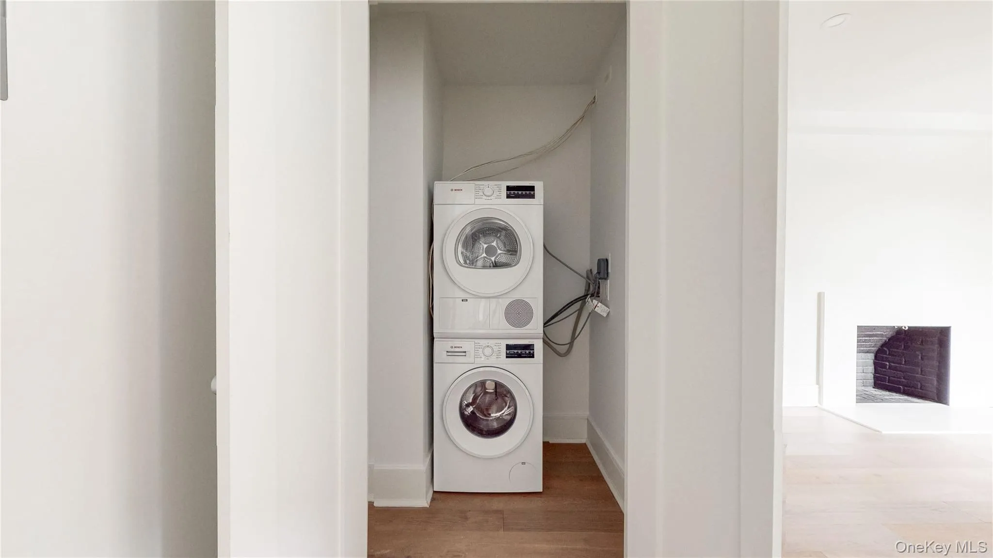 Stackable washer and dryer appliances, wood-finish flooring, and a fireplace with a brick interior Stackable washer and dryer appliances, wood-finish flooring, and a fireplace with a brick interior