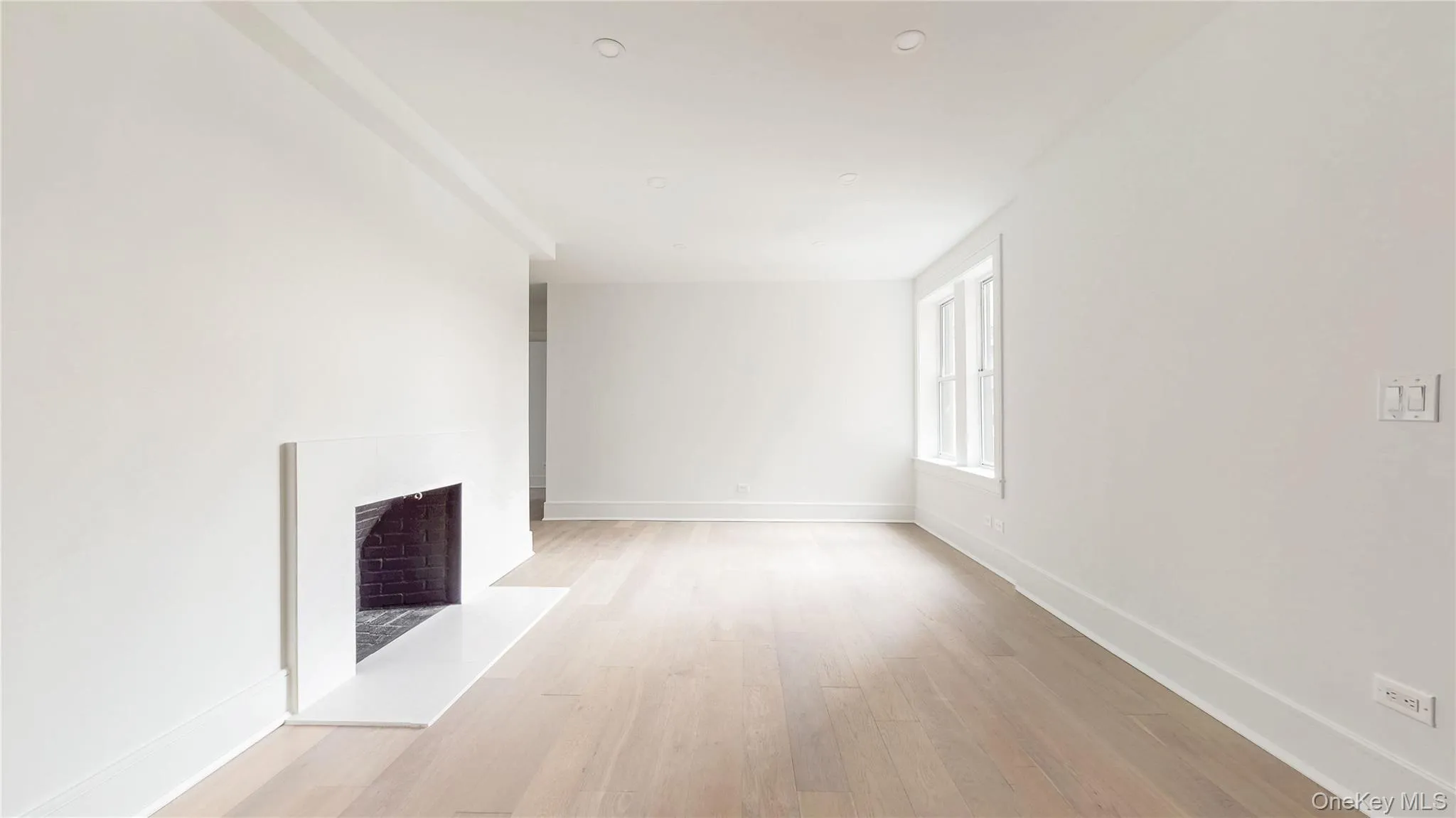 Recessed lighting, light wood-finish flooring, white trim, modern fireplace with a brick firebox, and multiple windows Recessed lighting, light wood-finish flooring, white trim, modern fireplace with a brick firebox, and multiple windows