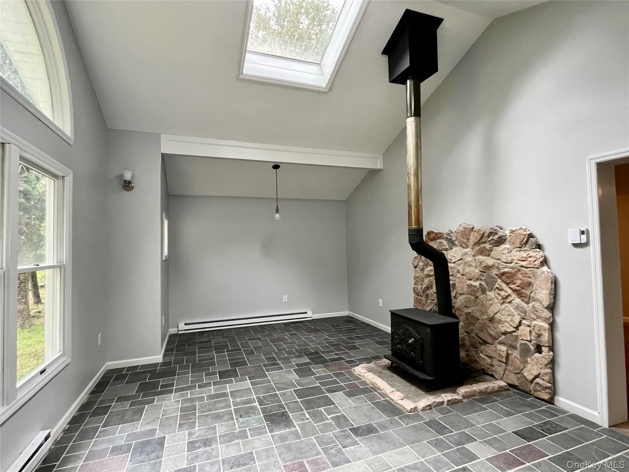Vaulted ceiling, skylight, wood-burning stove with stone surround, slate-style tile flooring, and arched window Vaulted ceiling, skylight, wood-burning stove with stone surround, slate-style tile flooring, and arched window
