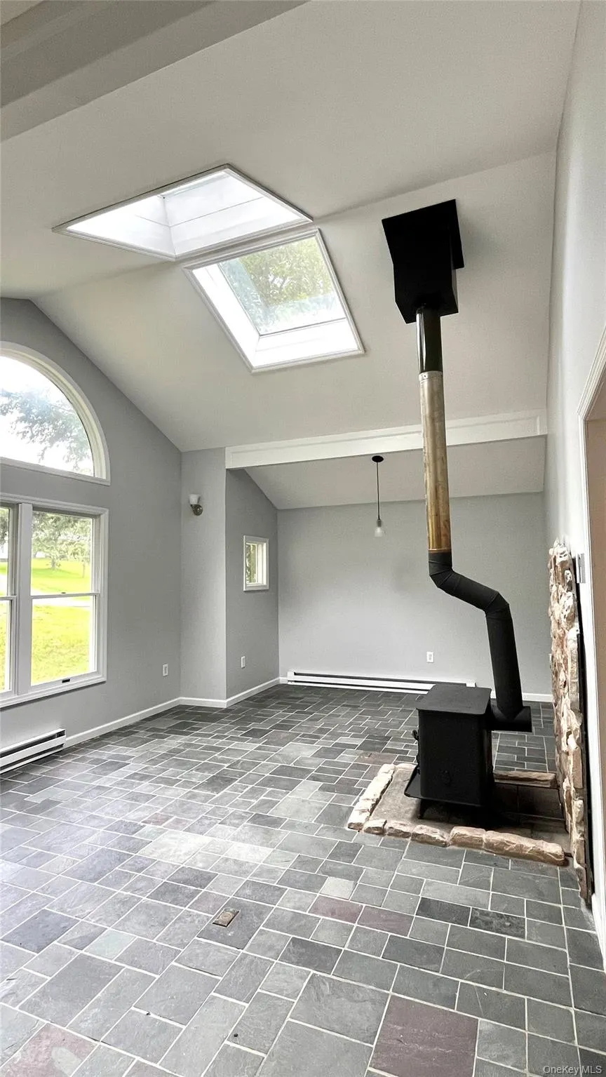 Vaulted ceiling with dual skylights, stone tile flooring, wood-burning stove with stone hearth, and an arched window Vaulted ceiling with dual skylights, stone tile flooring, wood-burning stove with stone hearth, and an arched window
