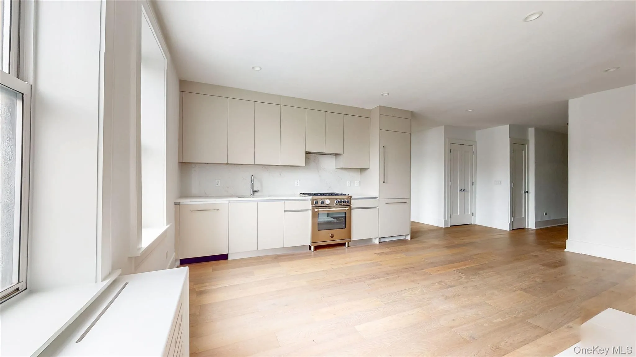 Kitchen with light wood-finish flooring, integrated panel-ready refrigerator, stainless steel range, and light-toned cabinetry Kitchen with light wood-finish flooring, integrated panel-ready refrigerator, stainless steel range, and light-toned cabinetry