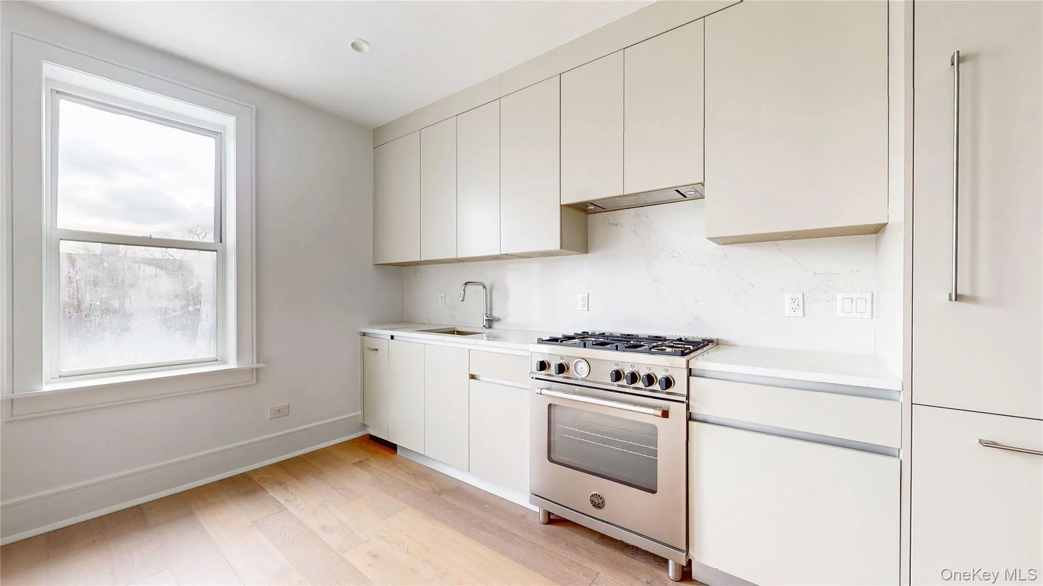 Modern kitchen featuring light-toned cabinetry, light wood-finish flooring, a stainless steel range, and a coordinated built-in refrigerator Modern kitchen featuring light-toned cabinetry, light wood-finish flooring, a stainless steel range, and a coordinated built-in refrigerator