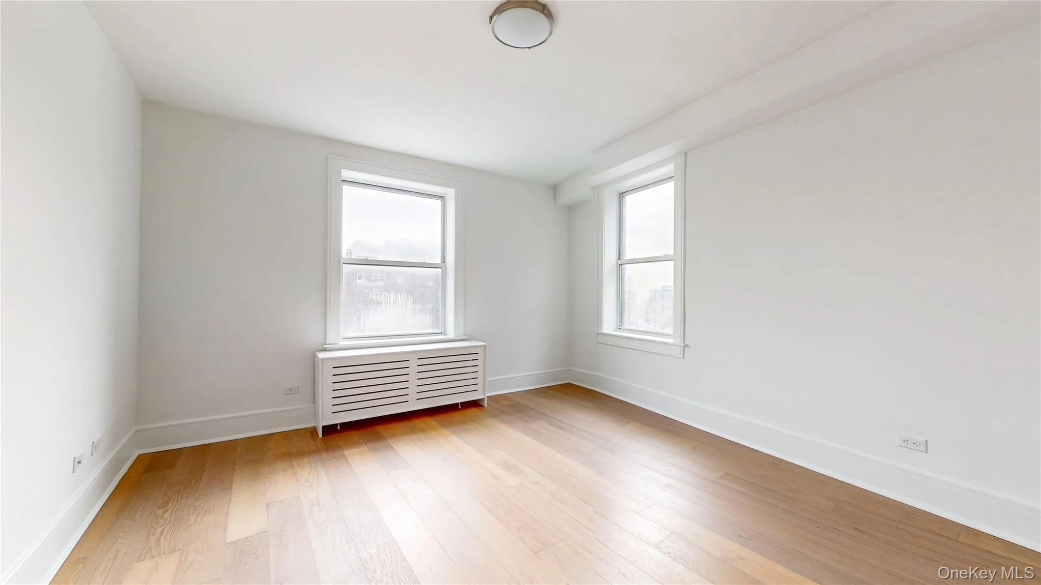 Wood-finish flooring, white walls, two windows, and a ceiling-mounted light fixture Wood-finish flooring, white walls, two windows, and a ceiling-mounted light fixture
