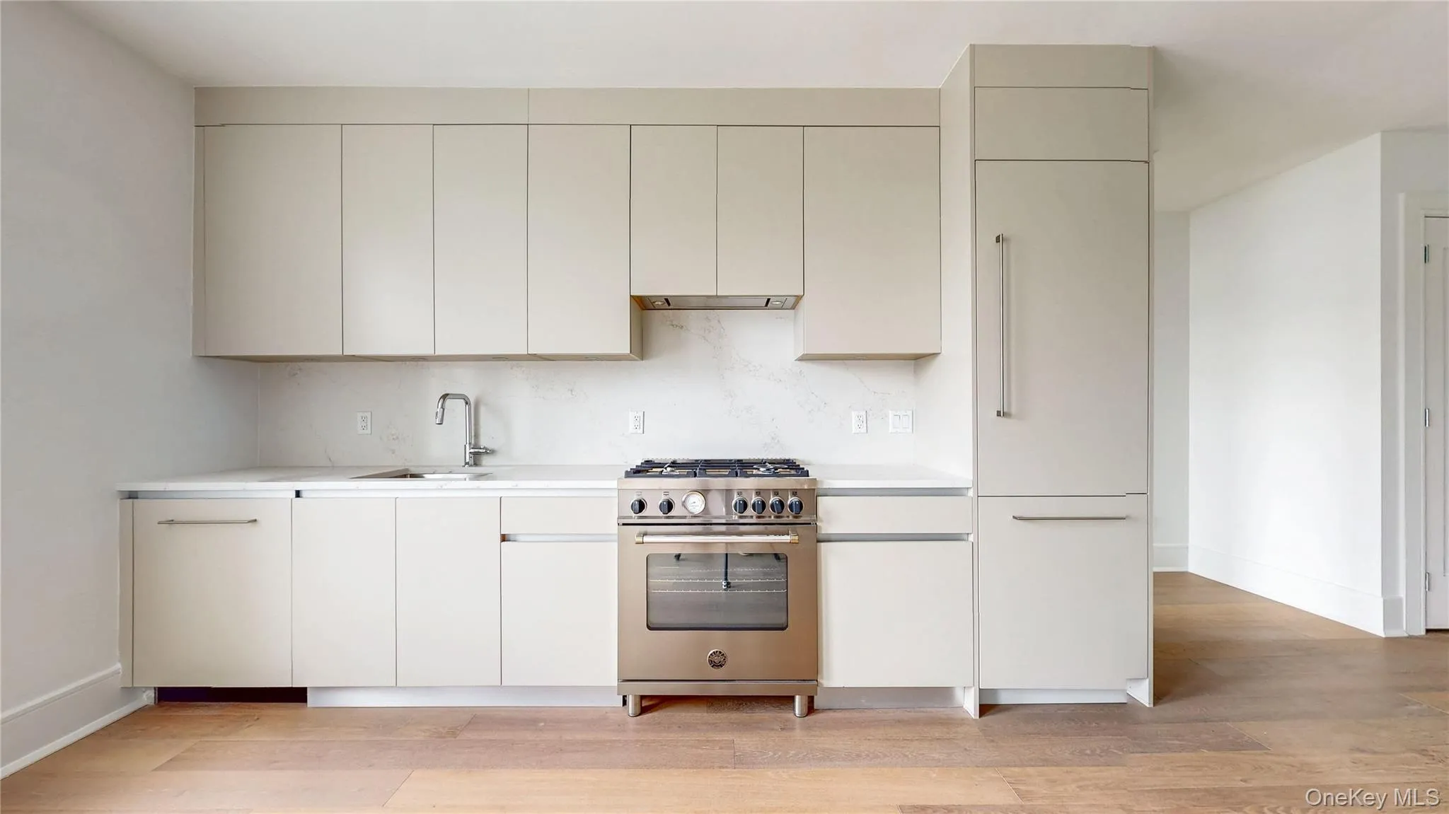 Modern kitchen featuring light-toned cabinetry, stainless steel appliances, a white countertop, and wood-finish flooring Modern kitchen featuring light-toned cabinetry, stainless steel appliances, a white countertop, and wood-finish flooring