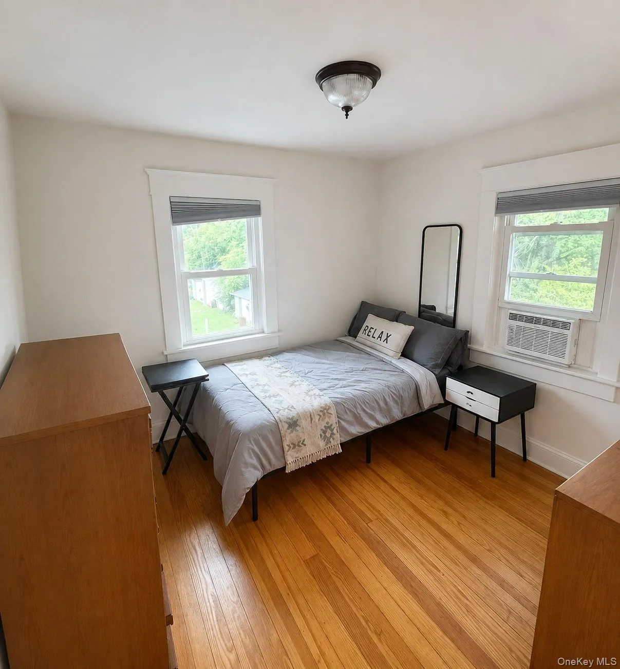 Hardwood flooring, two windows with window treatments, a flush mount ceiling light fixture, and white wall finishes Hardwood flooring, two windows with window treatments, a flush mount ceiling light fixture, and white wall finishes