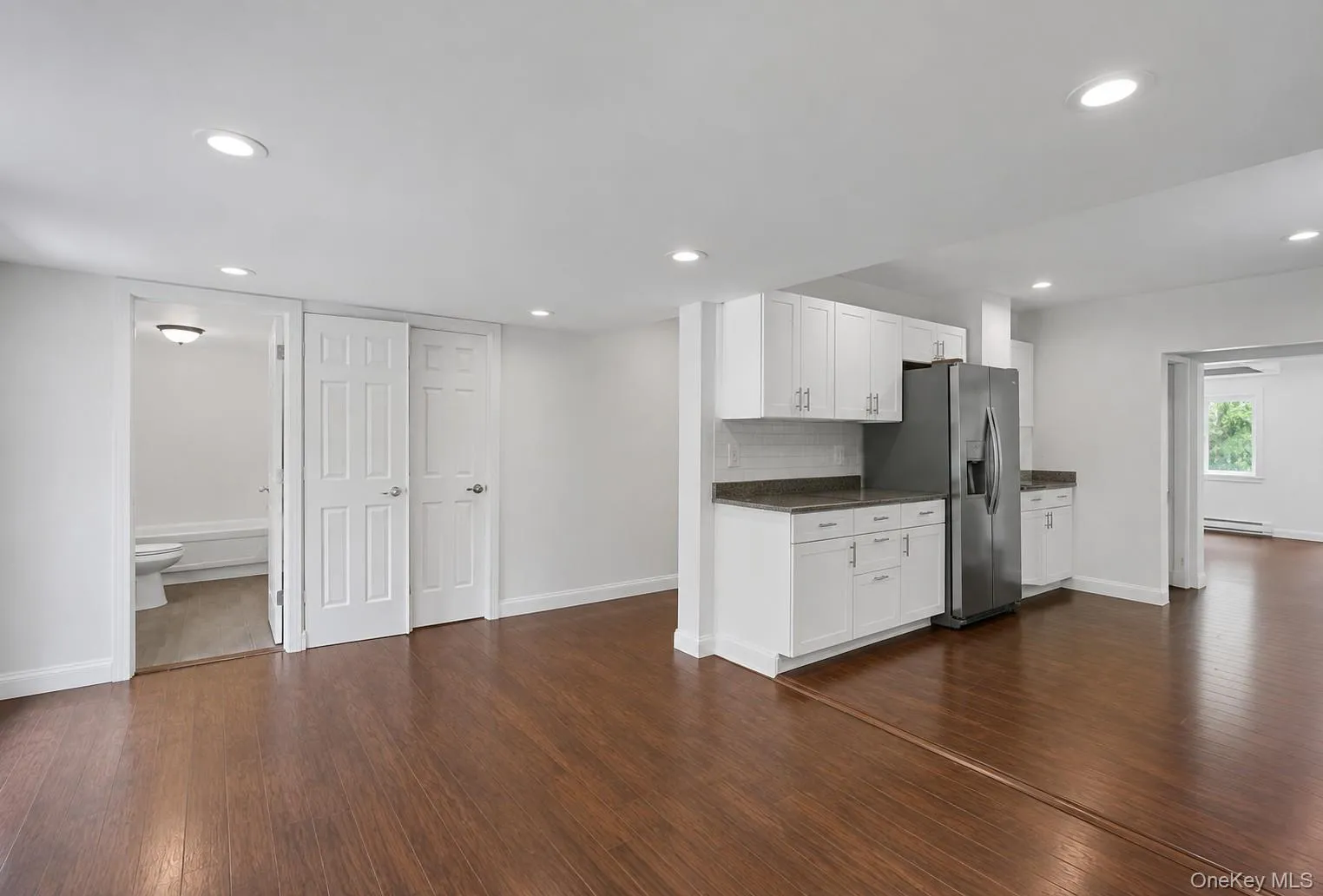 Wood-finish flooring throughout, recessed lighting, white kitchen cabinetry with stainless steel appliances, and a tiled backsplash Wood-finish flooring throughout, recessed lighting, white kitchen cabinetry with stainless steel appliances, and a tiled backsplash