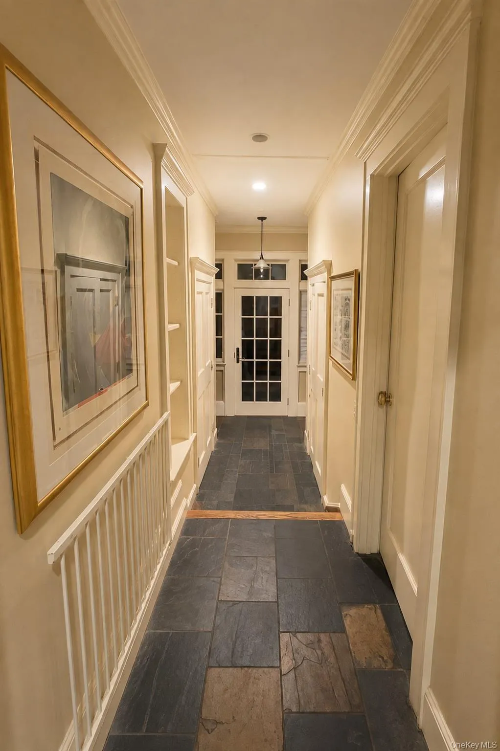 Hallway featuring mixed-tone slate flooring, built-in shelving, crown molding, and a grid-paned entry door with transom Hallway featuring mixed-tone slate flooring, built-in shelving, crown molding, and a grid-paned entry door with transom