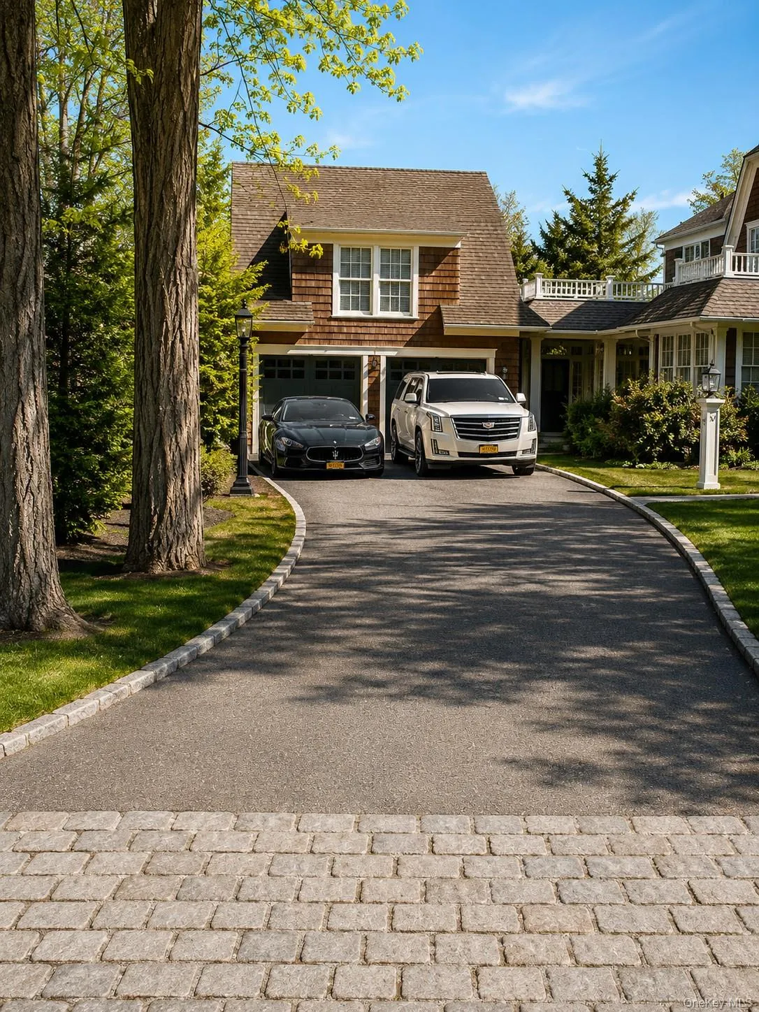 Asphalt driveway with stone paver apron, two-car garage, shingle siding, and dormer window Asphalt driveway with stone paver apron, two-car garage, shingle siding, and dormer window
