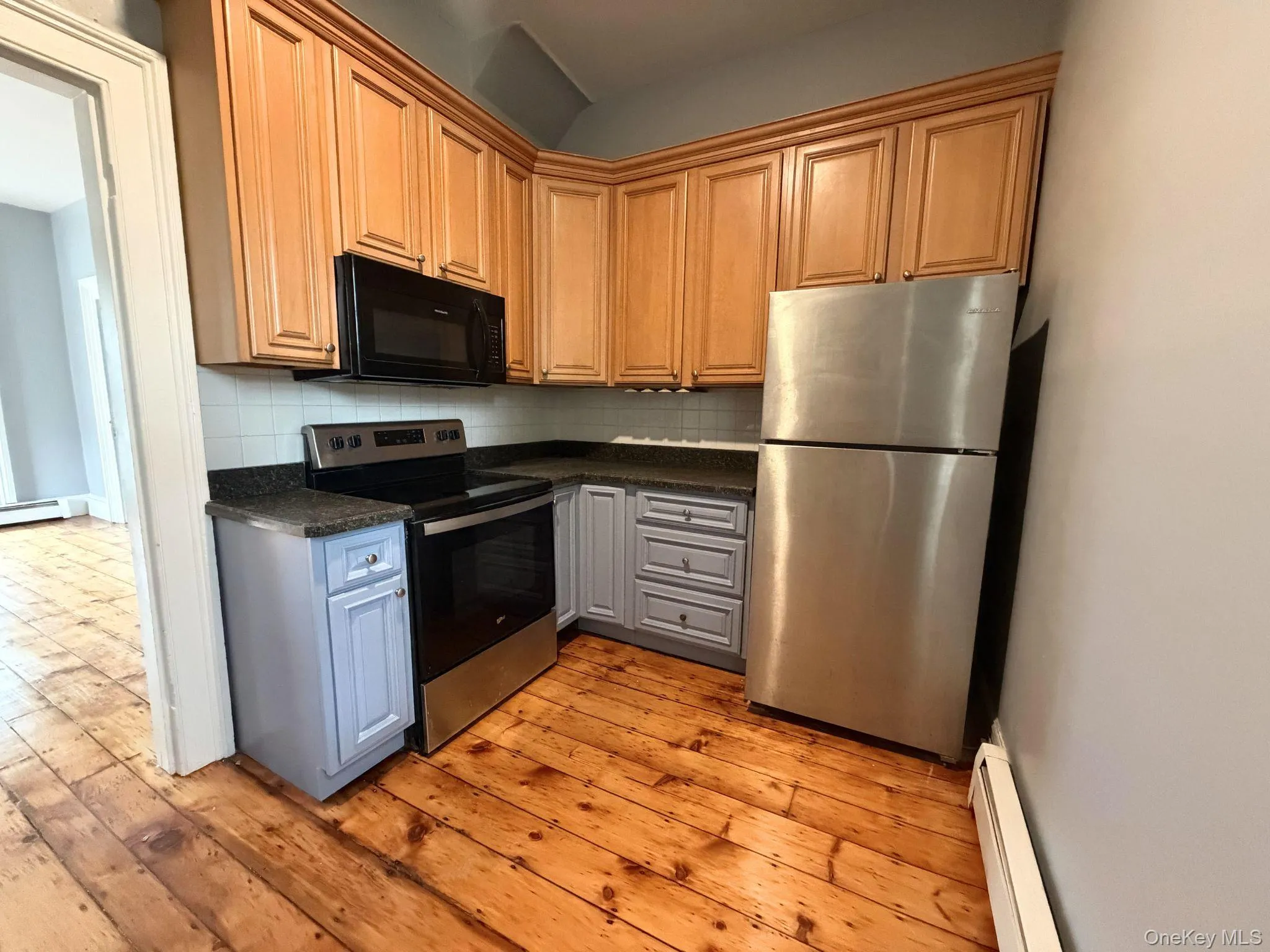 Kitchen featuring wood-finish upper cabinetry, stainless steel appliances, granite-style countertops, and a tile backsplash Kitchen featuring wood-finish upper cabinetry, stainless steel appliances, granite-style countertops, and a tile backsplash